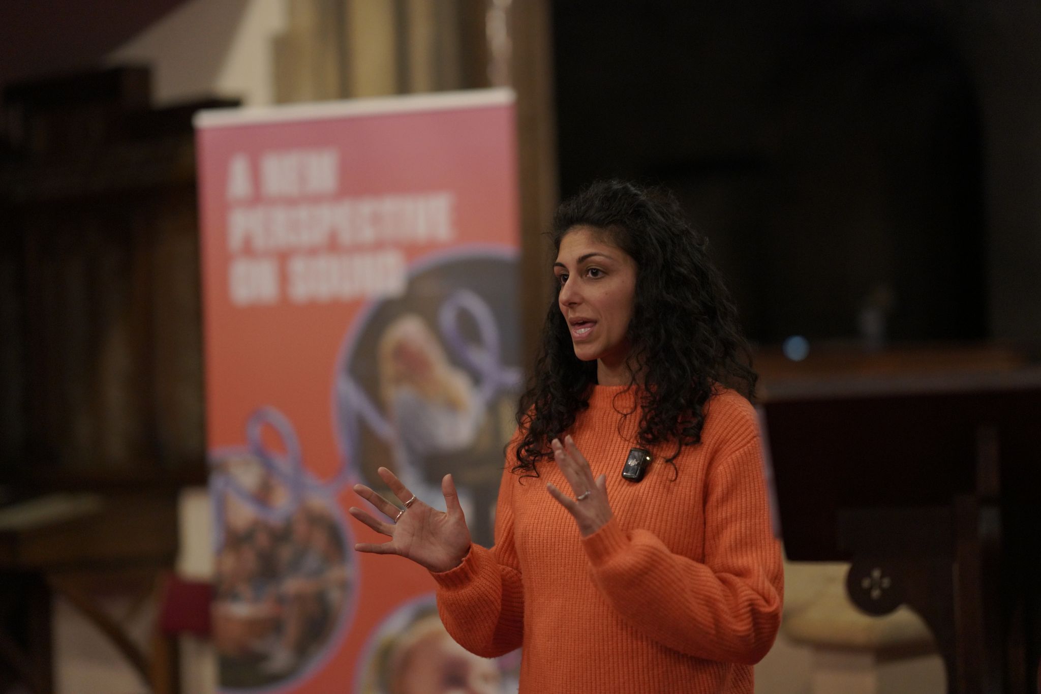 Speaker presenting at Sownd Affects hearing and wellness festival, with branded Sownd Affects banner blurred in the background.