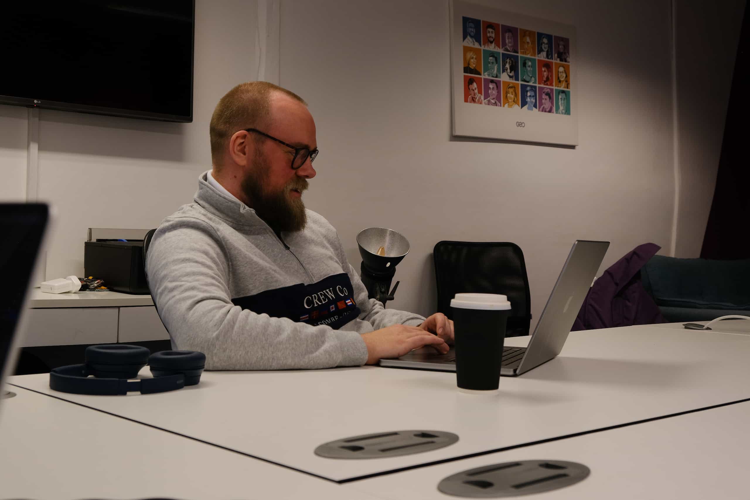 Charles, a developer, working on a laptop at a desk in a modern office with a coffee cup nearby.