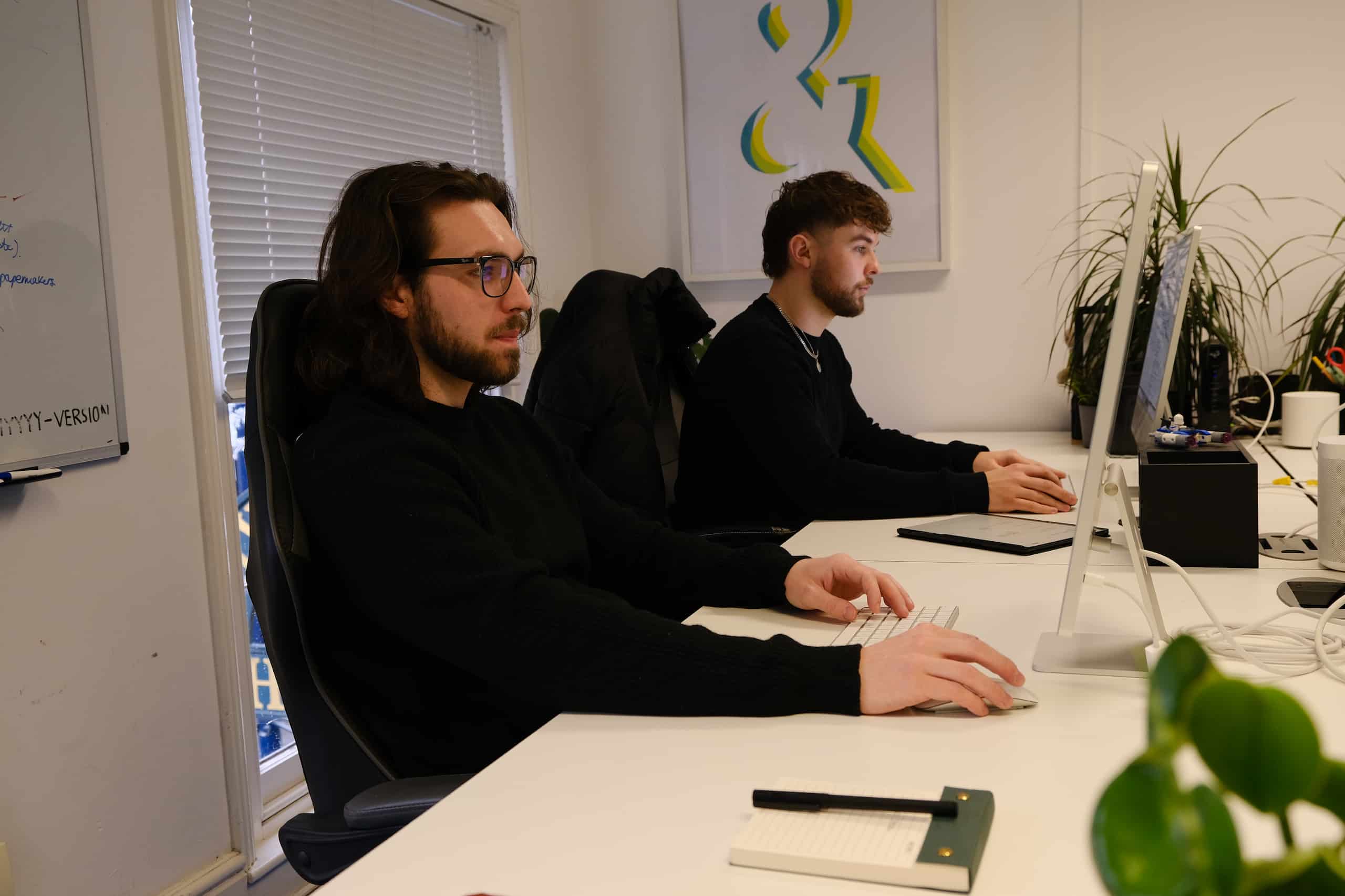 Spike and Kian – Developers Working at Their Desks Developers Spike and Kian working at desktop computers in a bright office workspace.